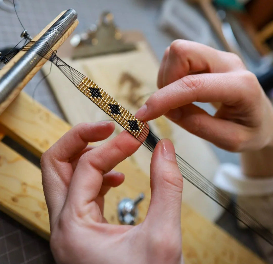 Hands weaving a gold and black star pattern on a bead loom at a workshop at Matty Miller Studio in Denver